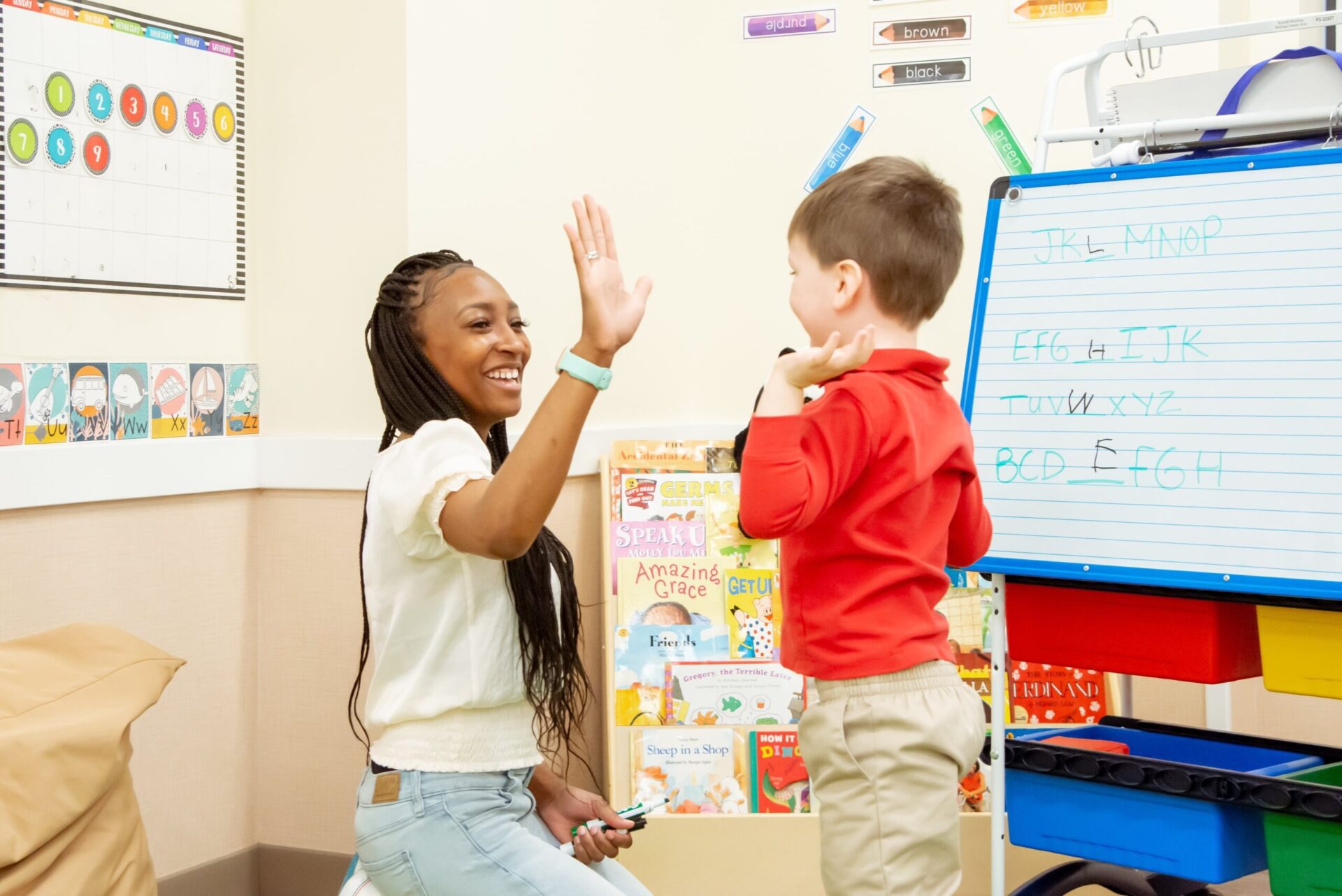 teacher high fiving preschooler near whiteboard alphabet activity