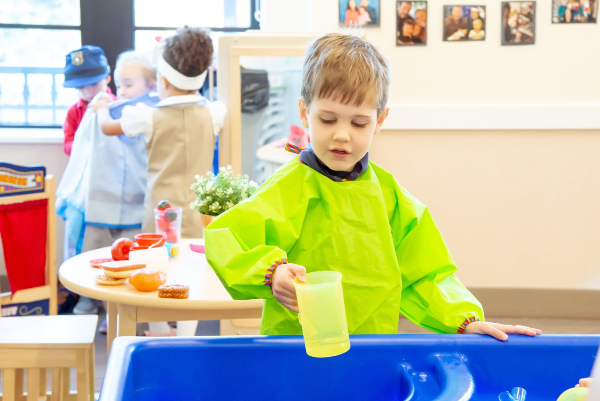 preschooler wearing green smock using cup to play in water
