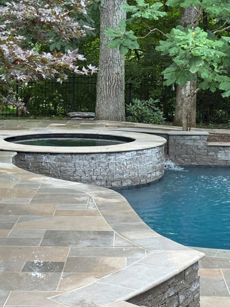 Stacked-stone raised spa spilling into the pool with a limestone deck