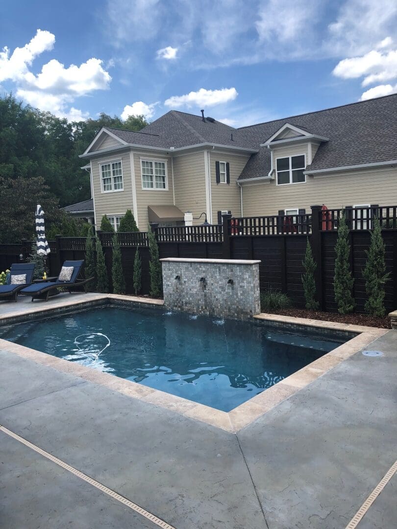 Rectangular pool with a stone water feature and privacy fence