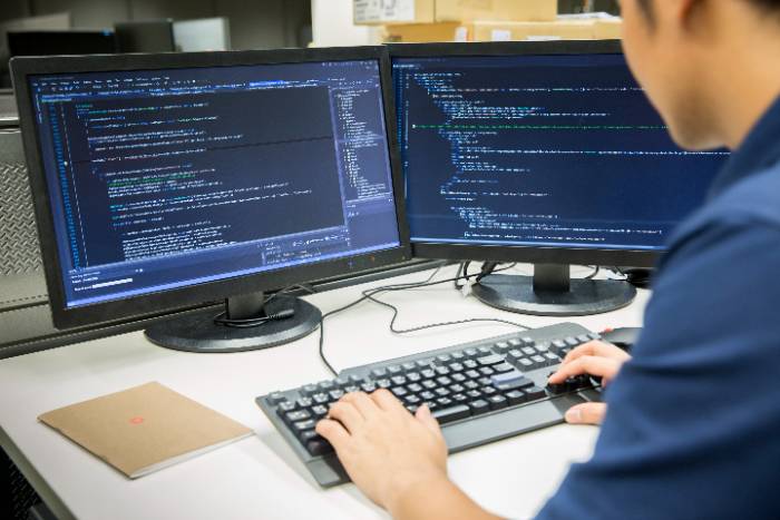 a student typing on a computer with a computer screen containing coding
