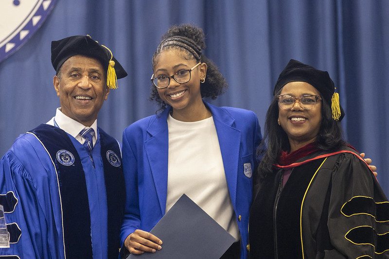 three people wearing caps and gowns and one holding a paper