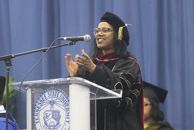 Dr. Jackson standing and speaking into a microphone wearing a cap and gown