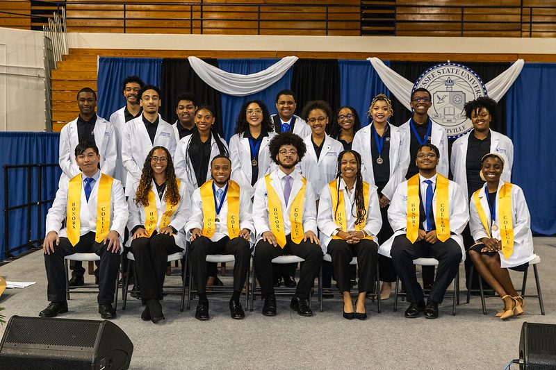 a group of students sitting down wearing honors stashes 