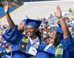 students raising their hands wearing caps and gown