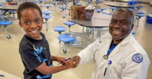 a nurse holding the hand of a child in a school cafeteria
