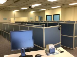 two computer monitors sitting on a desk in a room with cubicles 