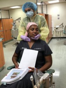 a dentist wearing a cap and mask with her hands around a patient's mouth